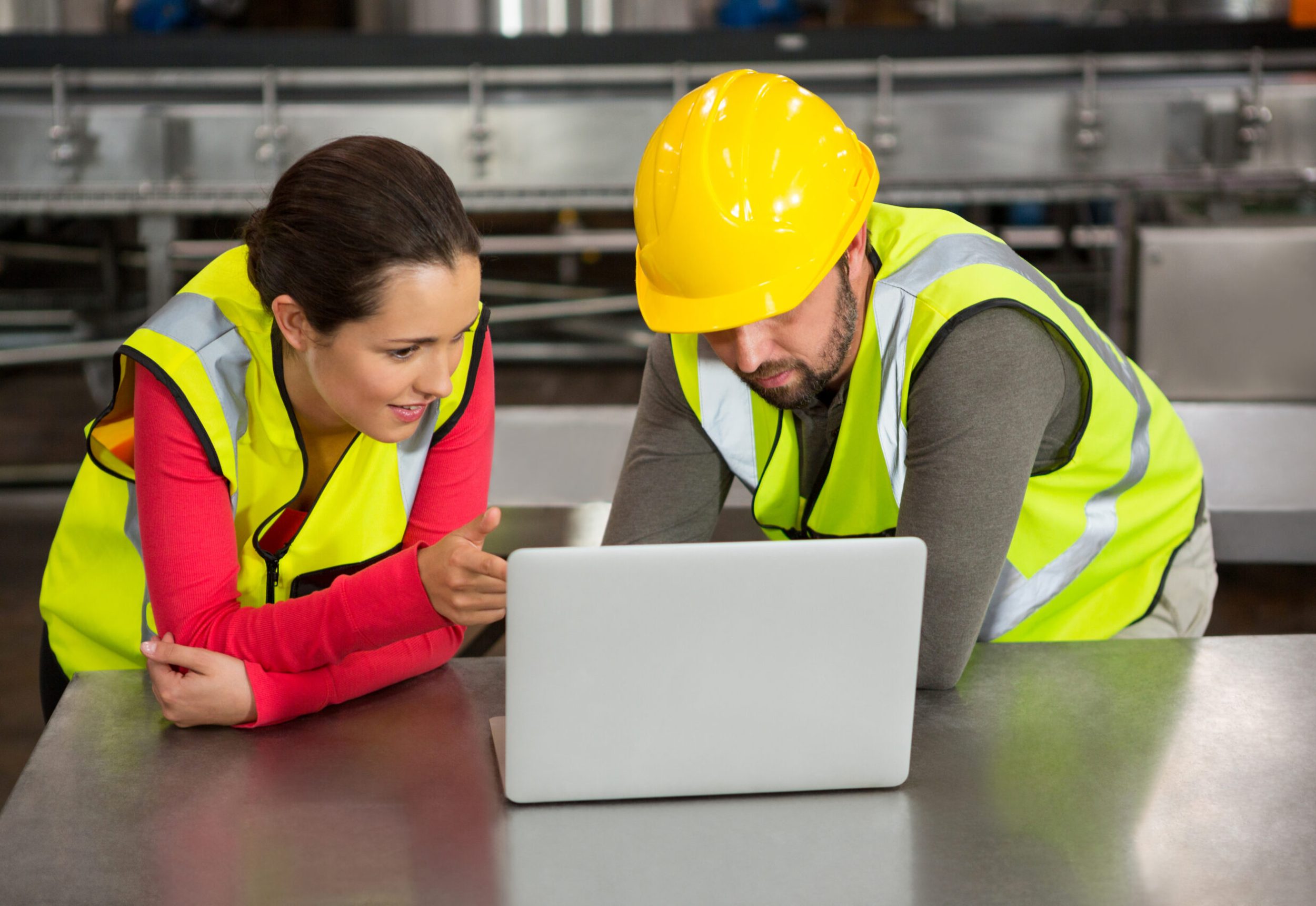 Male and female workers using laptop in factory