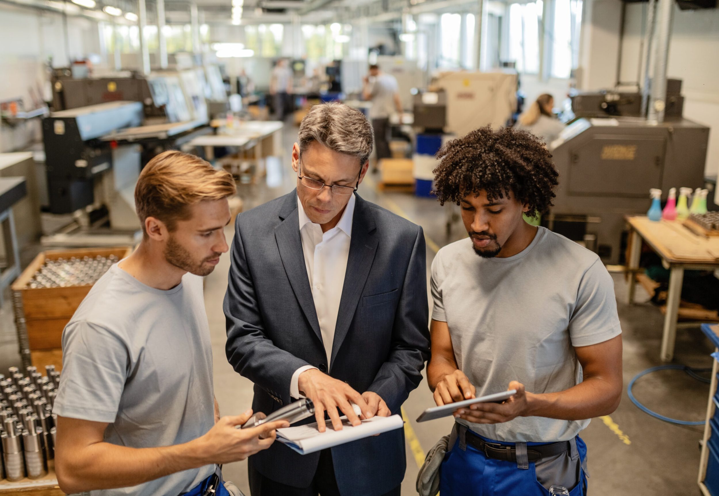 Mid adult engineer and two steel workers going through quality reports while working in industrial building.